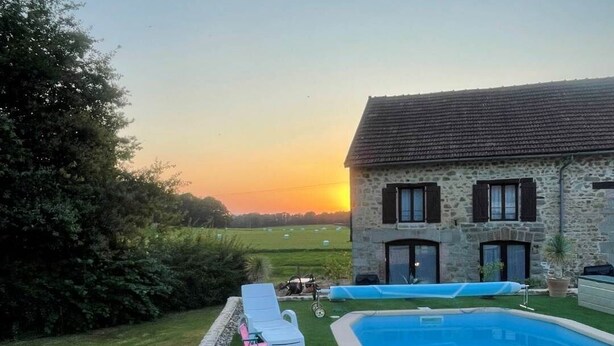 A stone house with a swimming pool, surrounded by a well-maintained lawn and a hedge.