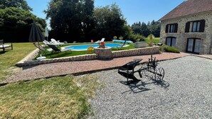A pool area with lounge chairs and umbrellas, surrounded by a stone wall and a gravel path.