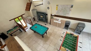 A pool table in a room with a staircase, a foosball table, and a map on the wall.