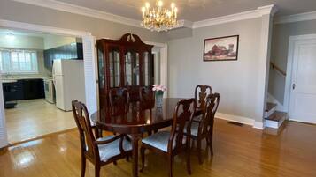 A dining room with a wooden table and chairs, a chandelier, and a painting on the wall.