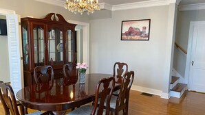 Un comedor con una mesa y sillas de madera, una araña y un cuadro en la pared.
