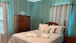 Una cama cuidadosamente tendida con una disposición de toallas en forma de cisne, una mesita de noche de madera, un armario de madera y un florero sobre el armario.