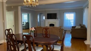 Comedor con una mesa redonda y sillas, una araña, una chimenea y un televisor montado encima.