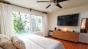 Une chambre à coucher avec un lit, une commode en bois, un téléviseur et un ventilateur de plafond.