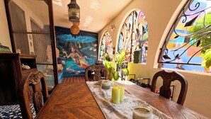 Un coin repas avec une table en bois, une nappe ornée de motifs d’étoiles de mer, des bougies et une fresque représentant une sirène.
