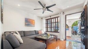 A living room with a gray sofa, a glass coffee table, a ceiling fan, and a view through a window to the outside. - Rachel’s Cove Room 2, Rachel's Cove - Room 2 The Mermaid and The Pearl Hotel (Isla Mujeres)
