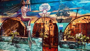 A mural with mermaid and pirate themes, a sign for 'The Mermaid and Pearl', and a storefront with arched entrances.