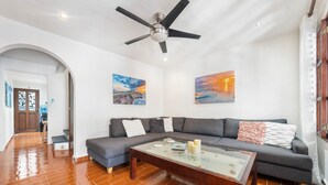A living room with a sofa, a coffee table, and two paintings on the wall. - Captain’s Quarters casita 2, Captain's Quarter - Casita 2 The Mermaid and The Pearl Hotel (Isla Mujeres)