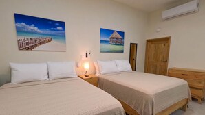 A bedroom with two beds, a nightstand, a wooden dresser, and wall-mounted air conditioning. - Captain’s Quarters casita 2, Captain's Quarter - Casita 2 The Mermaid and The Pearl Hotel (Isla Mujeres)