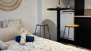A compact room with a bed, a kitchenette, and two stools. - Le - Studio - Louana (Aubusson)