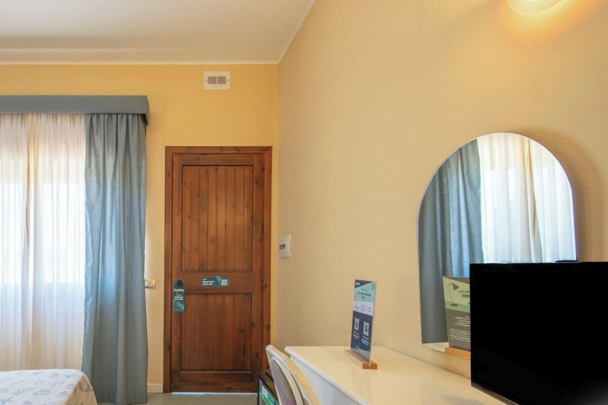 Una habitación de hotel con cama, escritorio, televisor, puerta y cortinas.