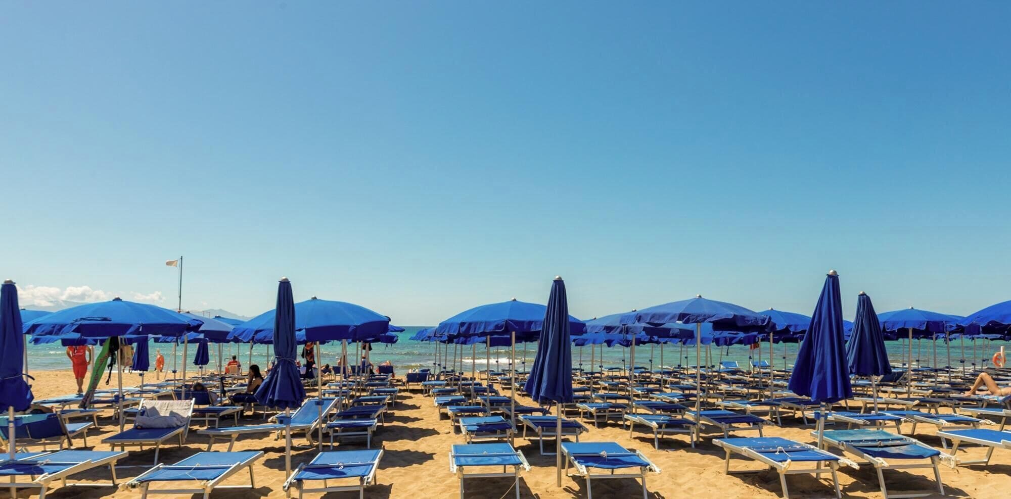 A beach with rows of blue sun loungers and matching umbrellas.