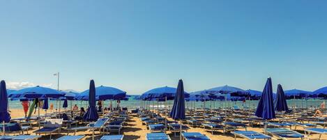 A beach with rows of blue sun loungers and matching umbrellas.