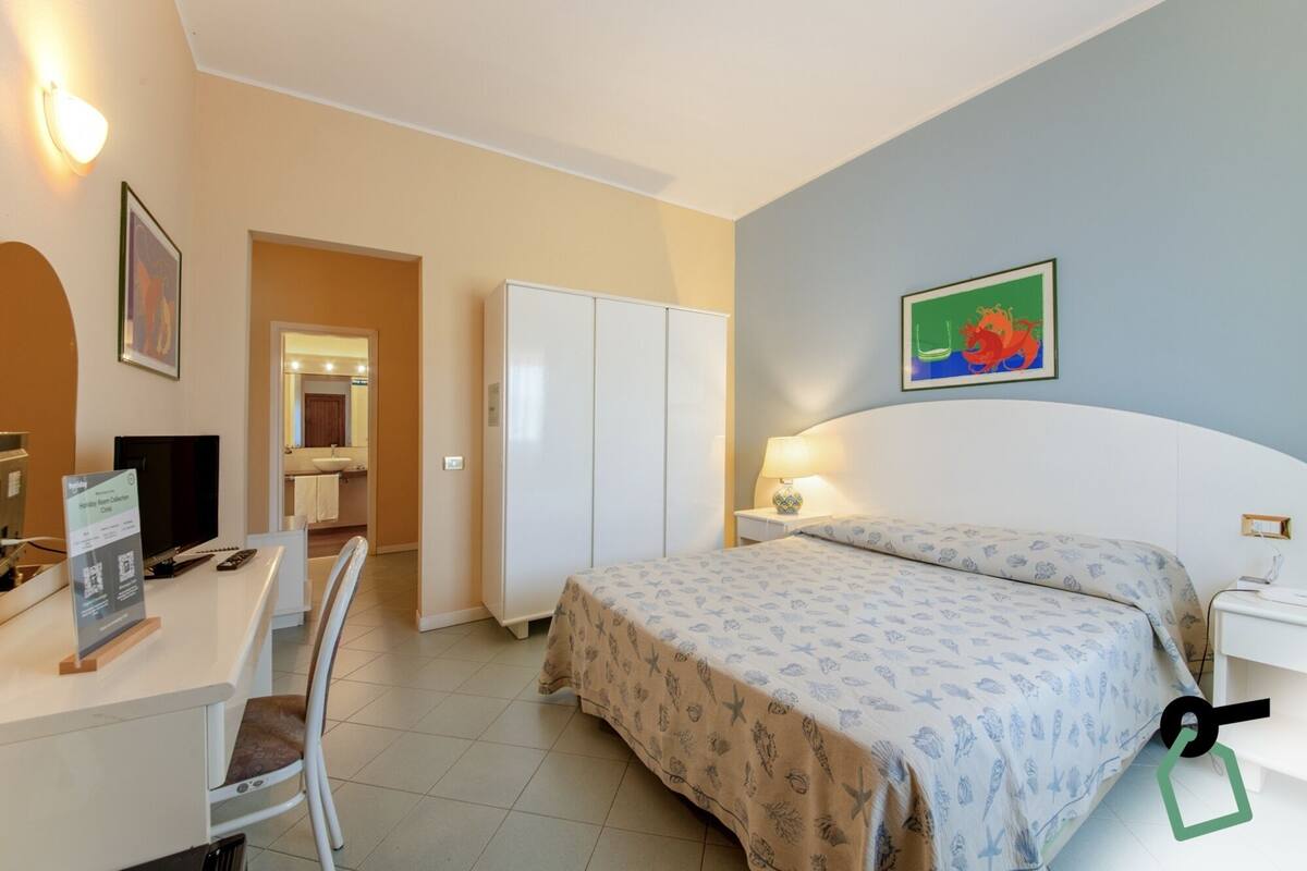 Habitación de hotel con cama, escritorio, silla y baño visible a través de una puerta abierta.