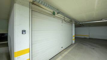 Un aparcamiento con una amplia puerta de garaje blanca marcada con franjas amarillas y un letrero verde que indica el número del garaje.