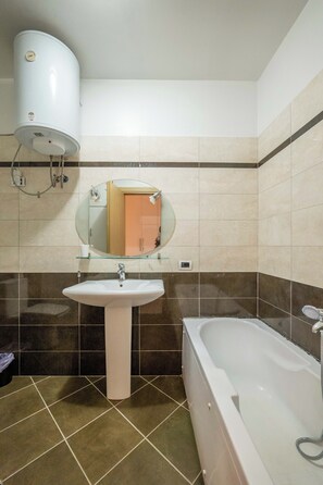 Une salle de bain avec un lavabo blanc, un miroir encadré de verre, une baignoire blanche et un radiateur fixé au mur.