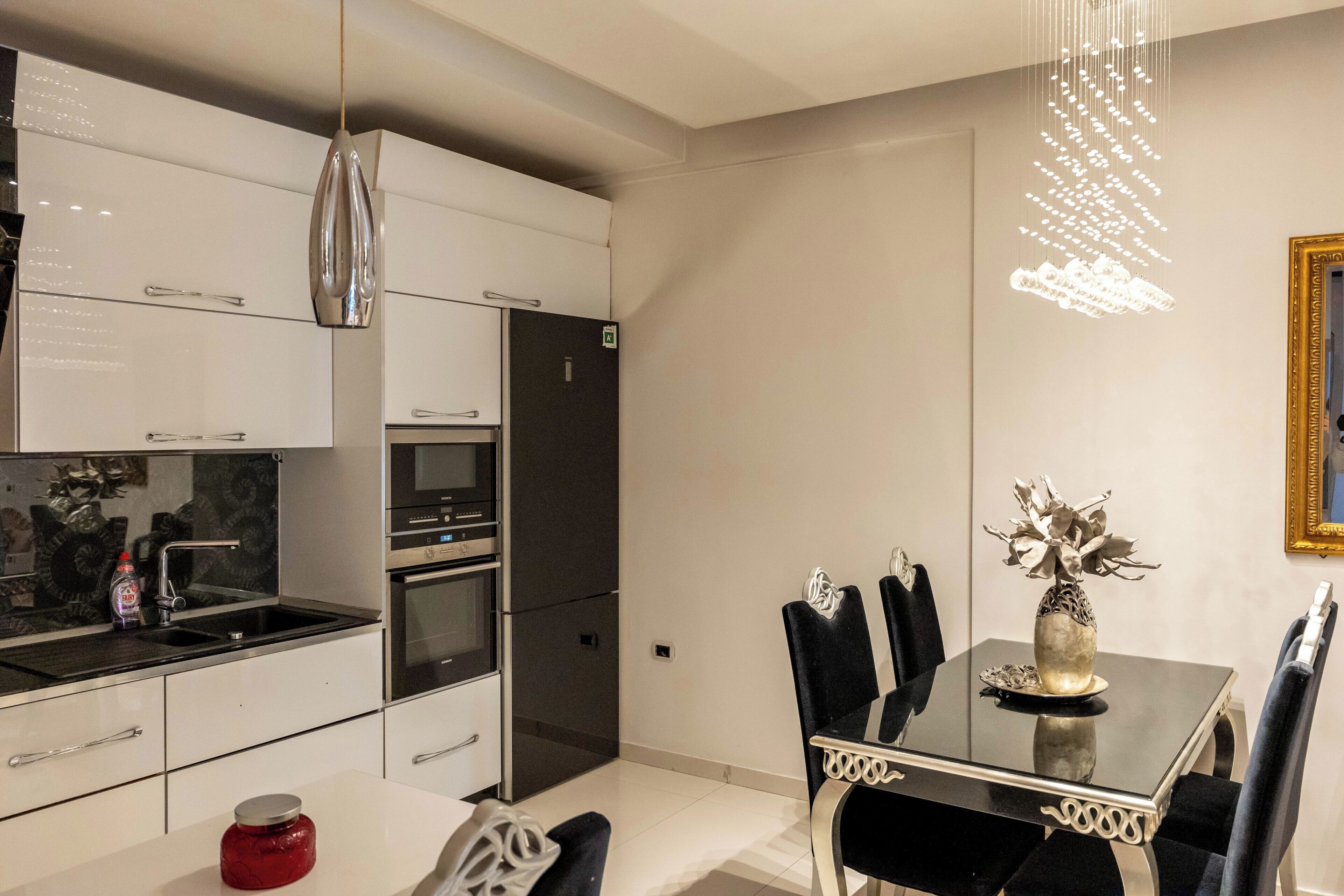 A modern kitchen with white cabinets, a black countertop, and a dining area with a glass table and black chairs.