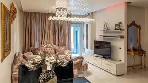 Una sala de estar moderna con una araña, un conjunto de sofá, un televisor y un espejo decorativo.