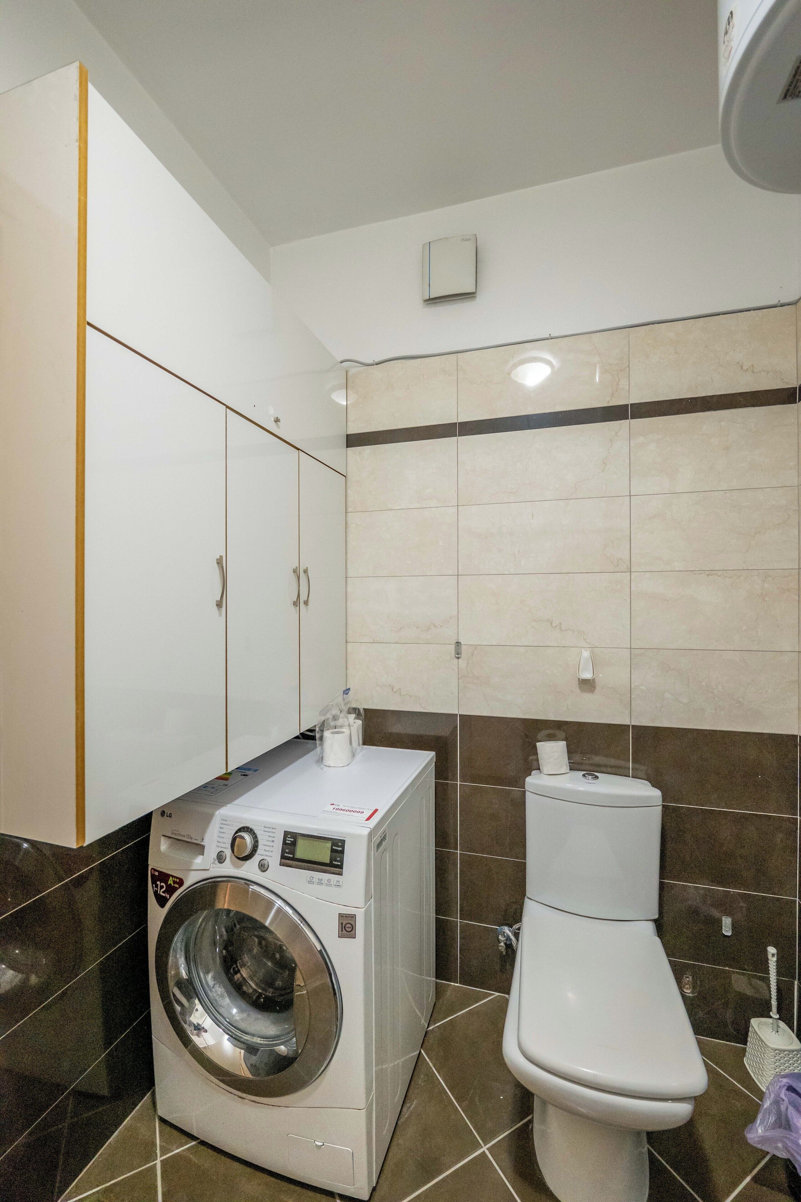 Un baño pequeño con lavadora, inodoro y paredes de azulejos.