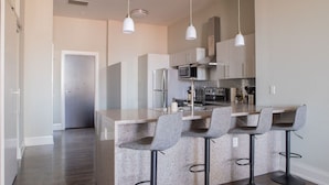 A modern kitchen with a granite island, bar stools, stainless steel appliances, and pendant lighting.