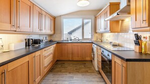 Una cocina moderna con armarios de madera, encimera negra, horno empotrado y ventana que deja entrar luz natural.