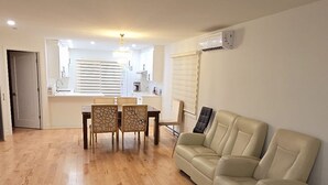 Un vaste espace de vie doté d’un plancher en bois, d’un canapé beige, d’une table à manger avec des chaises, et d’une cuisine à l’arrière-plan.