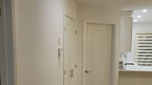 Un couloir doté d’un plancher en bois, de murs blancs et d’une porte donnant sur une salle de bain équipée d’un lavabo et d’un miroir.