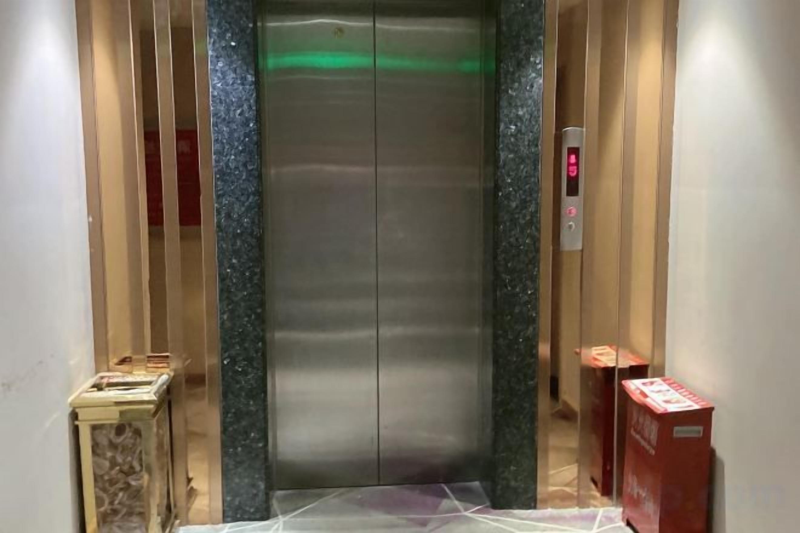 An elevator with a metallic interior, a control panel with a red button, and a green light indicator.
