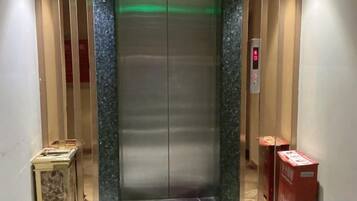 An elevator with a metallic interior, a control panel with a red button, and a green light indicator.