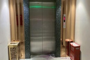 An elevator with a metallic interior, a control panel with a red button, and a green light indicator.
