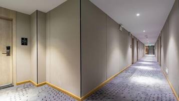 A long, narrow hotel corridor with a patterned carpet, a wooden door on the left, and a sign on the wall.
