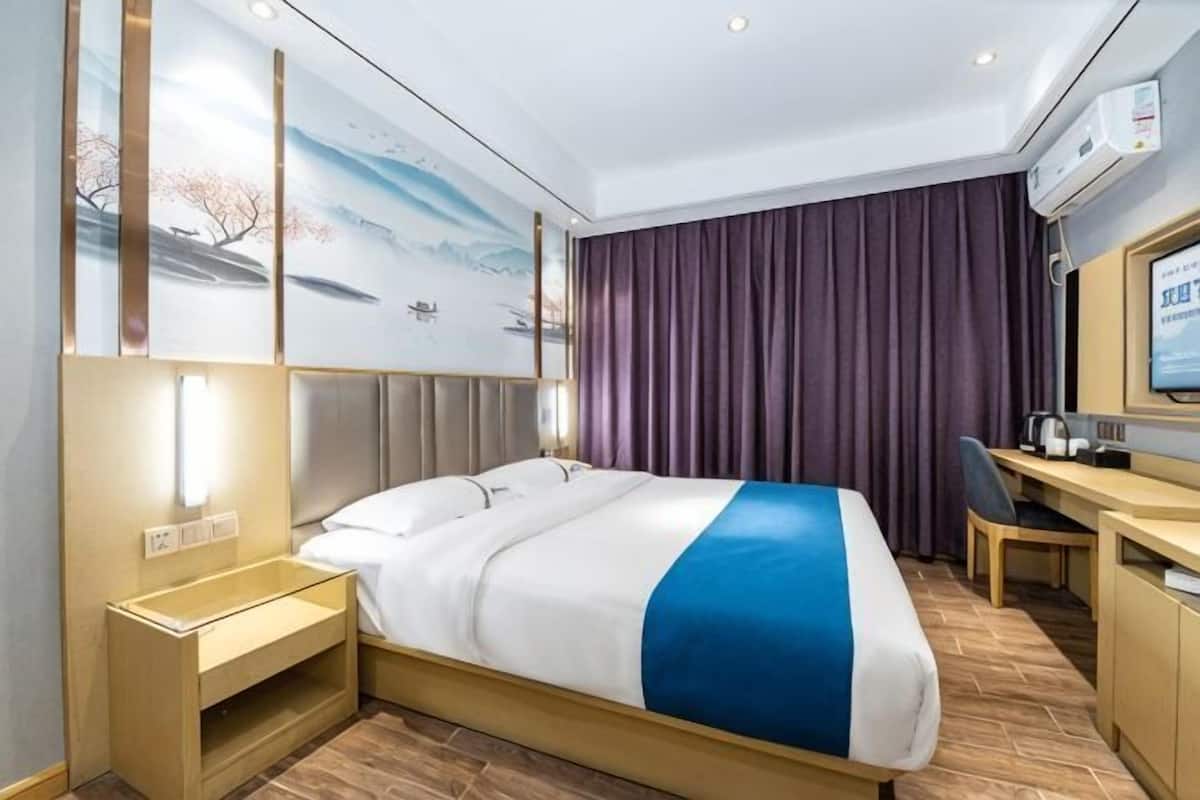 Una habitación de hotel con cama, mesita de noche, escritorio, silla y televisión.