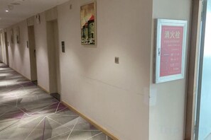 A corridor with a patterned carpet, framed artwork on the walls, and a sign with text.