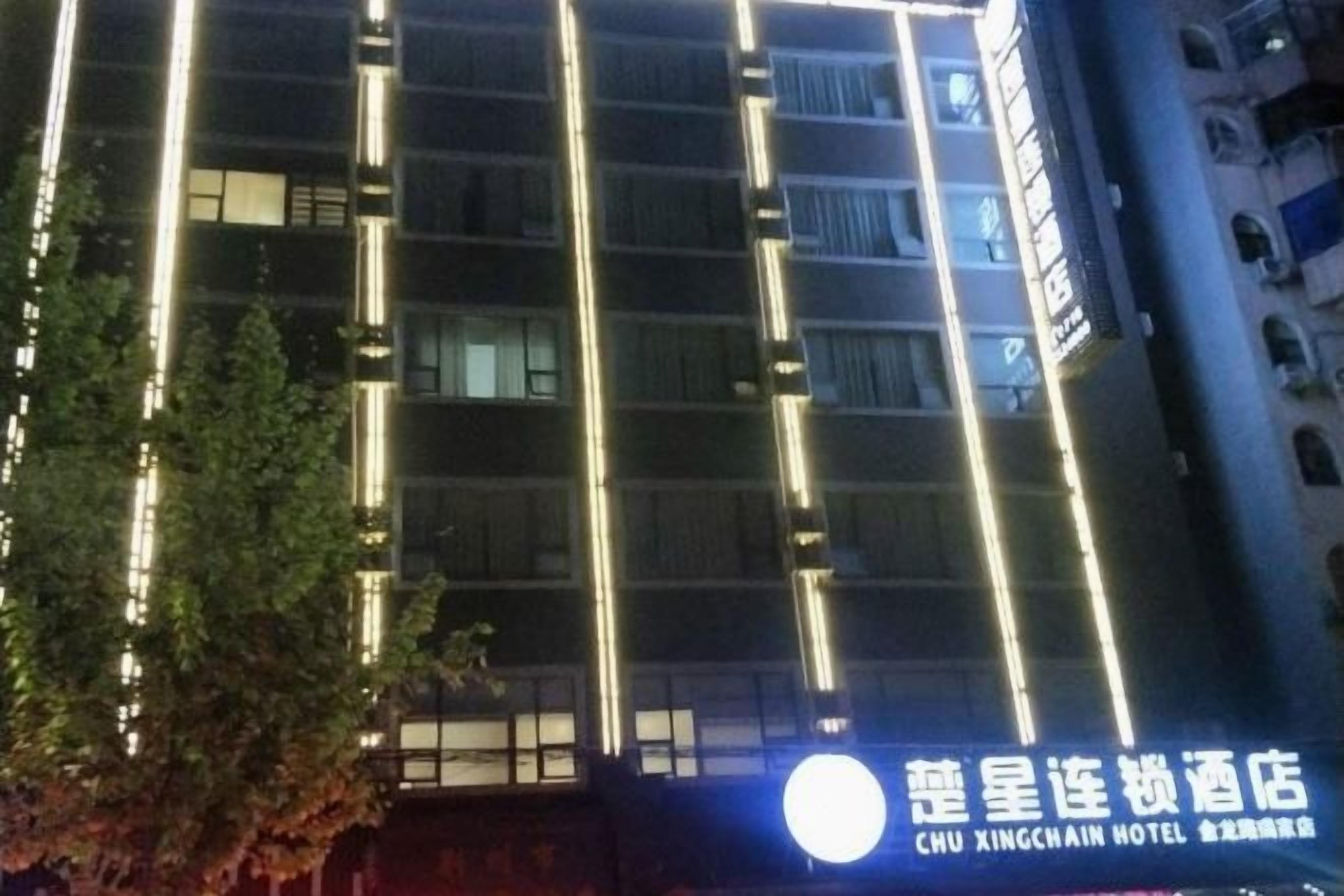 A multi-story hotel building with illuminated vertical lines on the facade, a visible sign with Chinese characters, and a tree in the foreground.
