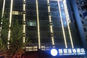 A multi-story hotel building with illuminated vertical lines on the facade, a visible sign with Chinese characters, and a tree in the foreground. - Rui Jia Business Hotel (Jingzhou)