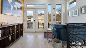 A modern living room with a large world map on the wall, a blue sofa, a bookshelf, and a glass coffee table. - 10-Min to ABIA, UT, Downtown Bright & Dog-Friendly w Fenced Yard 2-Car Parking (Austin)