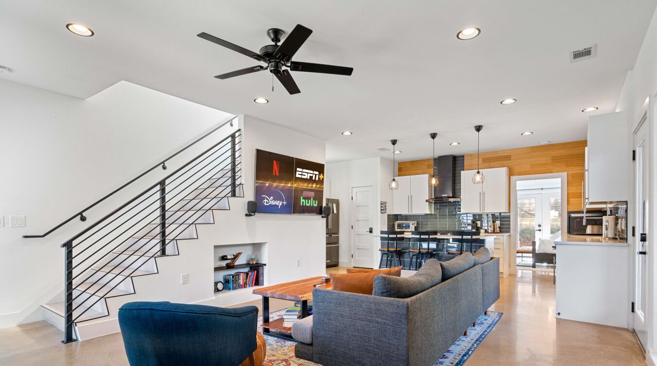 A modern living room with a staircase, a kitchen, and a dining area.