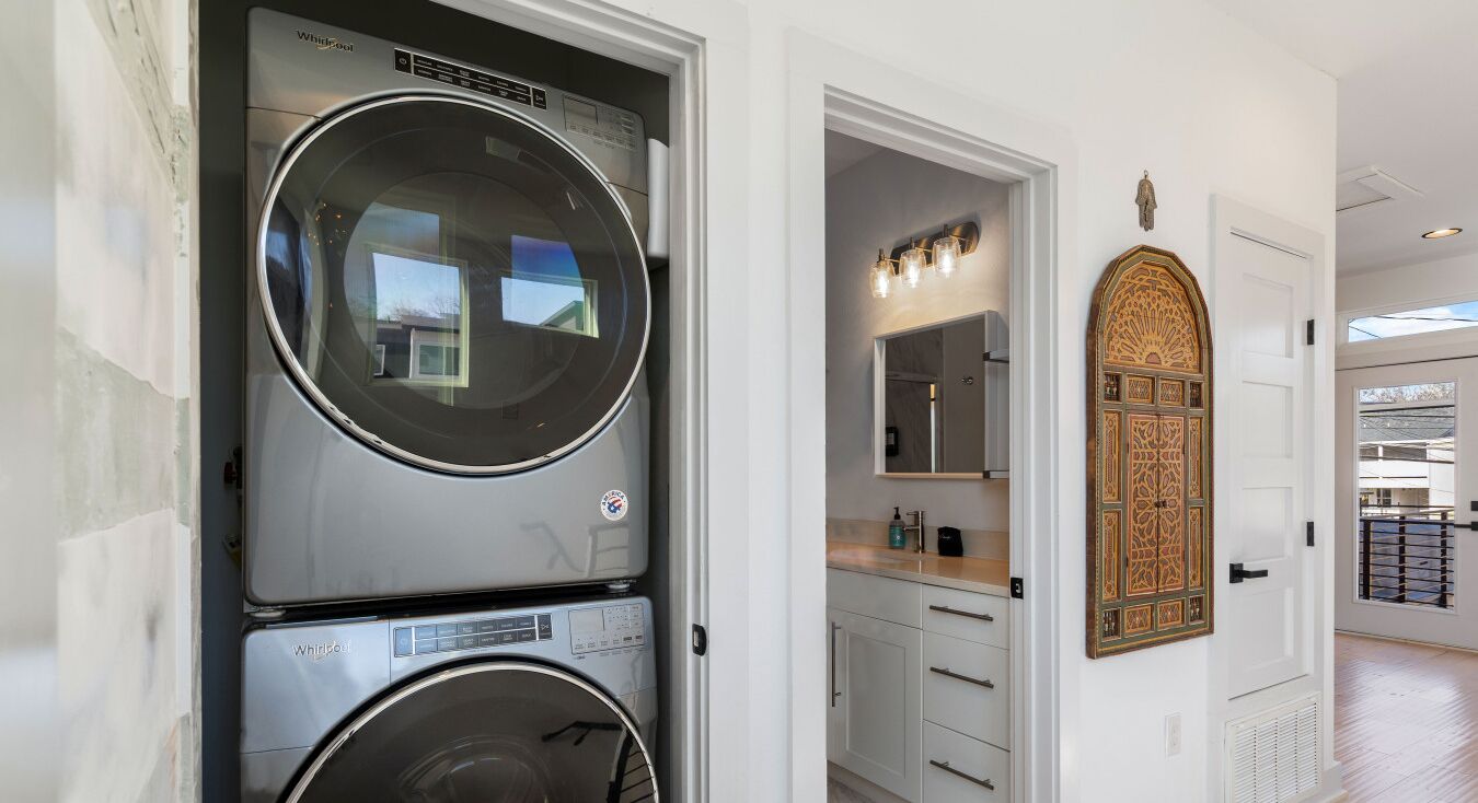 Uma lavanderia com máquinas de lavar e secar empilhadas, um lavatório com espelho e uma porta decorativa.