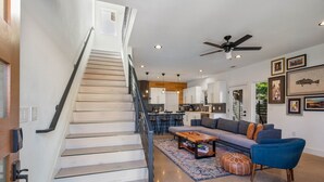A modern living space with a staircase, a kitchen, a dining area, and a seating area with a sofa and ottoman. - 10-Min to ABIA, UT, Downtown Bright & Dog-Friendly w Fenced Yard 2-Car Parking (Austin)