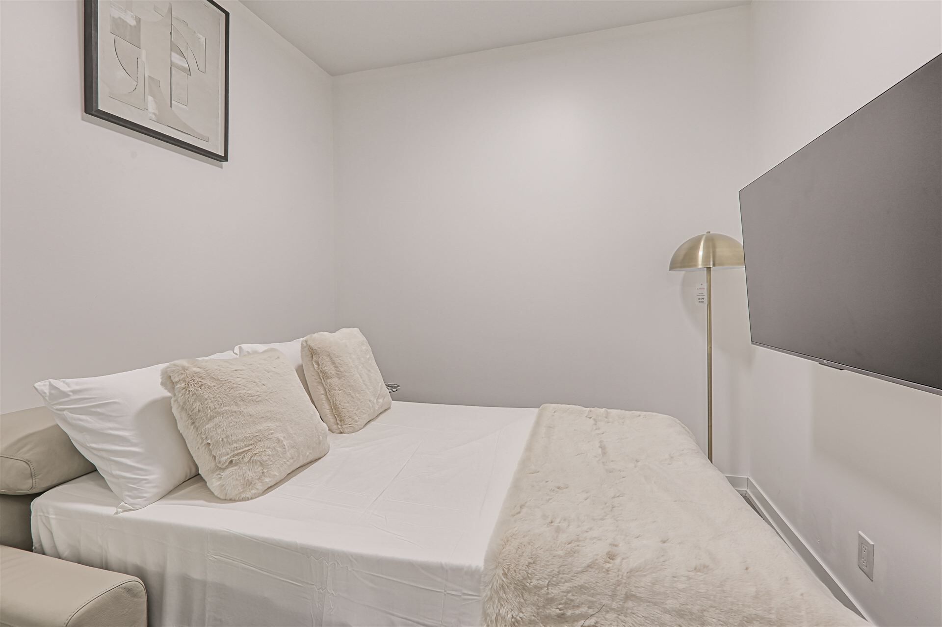 A bedroom with a bed, a bedside table, a lamp, and a wall-mounted TV.