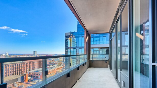 A balcony with a city view, featuring modern buildings and a clear sky.