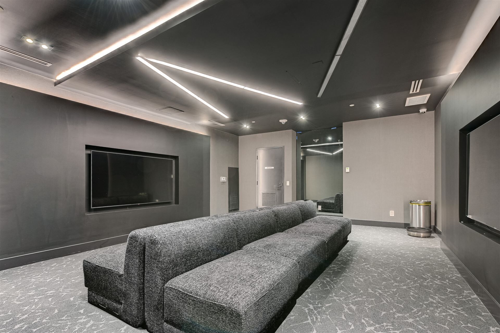 Une salle de cinéma maison moderne, dotée d’un grand téléviseur à écran plat, d’un canapé confortable de couleur grise et d’un sol recouvert de moquette.