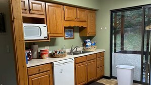 A compact kitchen with wooden cabinets, a microwave, a dishwasher, and a window overlooking a garden.