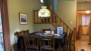 A dining area with a table and chairs, a chandelier, and a staircase leading to another room.