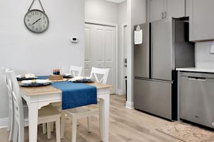 A modern kitchen with stainless steel appliances, a dining table set with white chairs, and a wall clock.