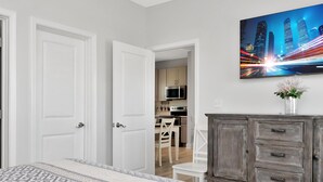 A bedroom with a patterned bedspread, a wooden dresser, and a cityscape painting on the wall. - Sea La (Port St. Joe)