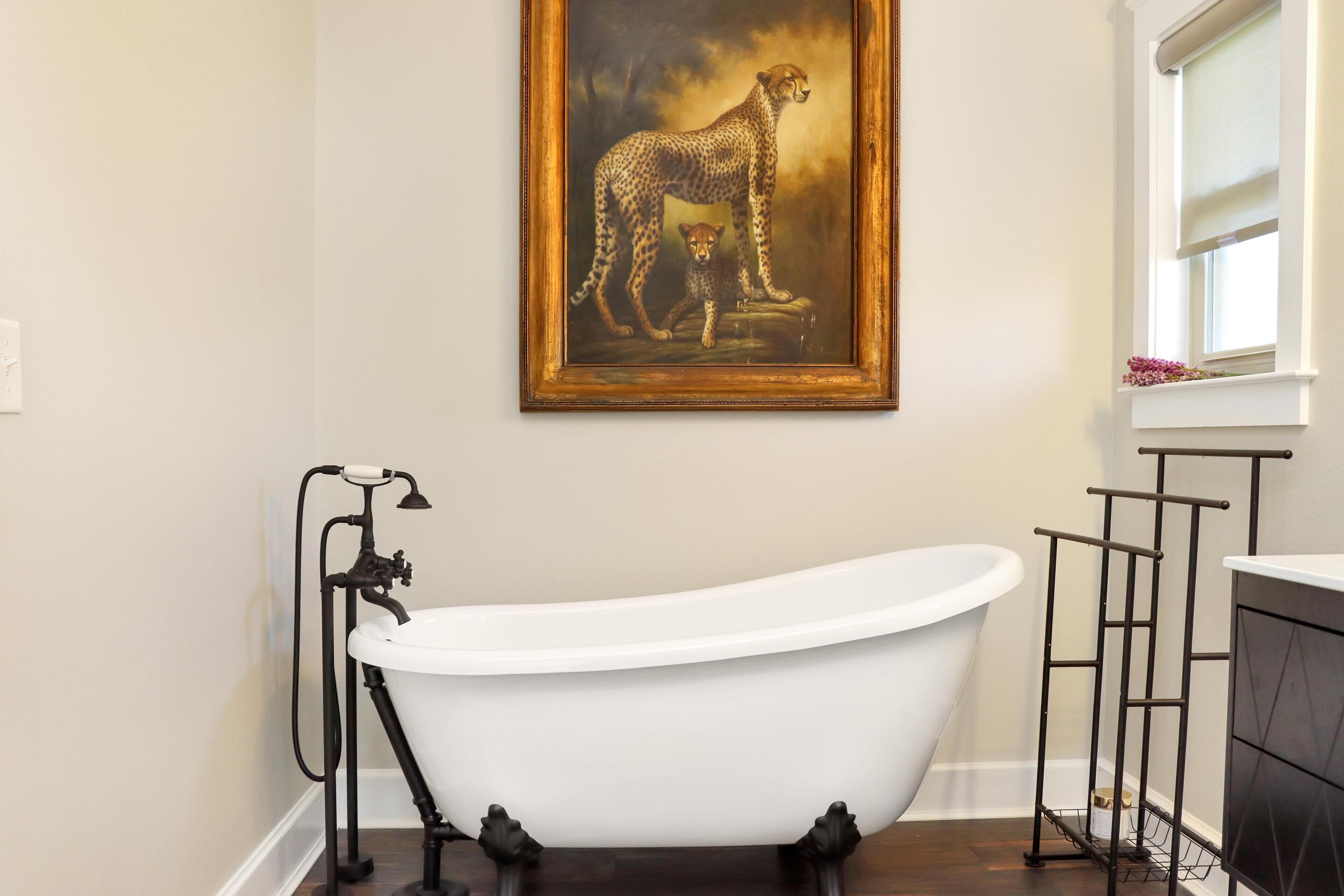 A bathroom with a freestanding bathtub, a vintage-style faucet, and a framed painting of a cheetah and cub.