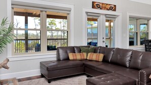 A modern living room with a sectional sofa, large windows, and a view of the outdoors. - Treetops (Port St. Joe)