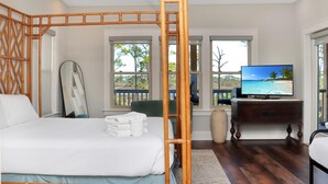 A bedroom with a bed, a television, a dresser, and a window with a view of palm trees. - Treetops (Port St. Joe)