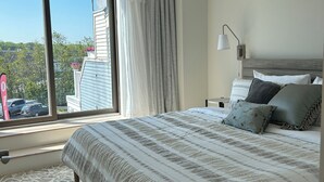 A bedroom with a large bed, a ceiling fan, a window with curtains, and a view of the outside. - Sunny downtown Belfast apartment with water view, right on Main St near eateries (Belfast)